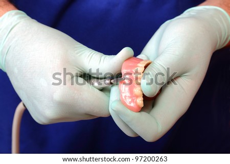 Doctor holding dental prosthesis and  tool in hads with protective gloves