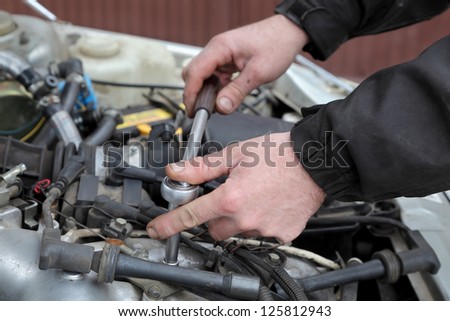 Modern car gasoline engine servicing, workers hands, ratchet and spark plug