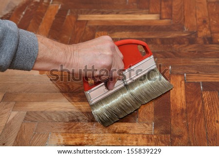 Varnishing of oak parquet floor, workers hand and brush
