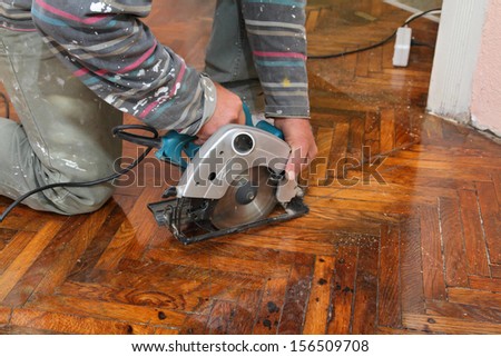 Worker cut old parquet floor with electric saw