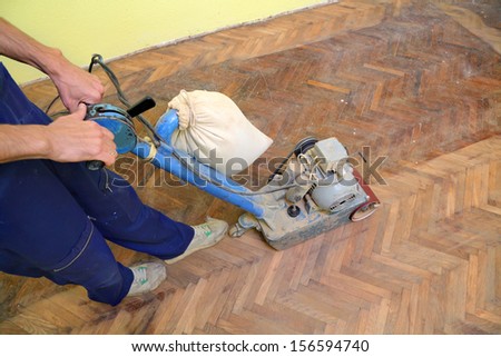 Worker polishing old parquet floor with grinding machine
