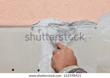Worker spreading plaster with trowel to gypsum board and fiber mesh
