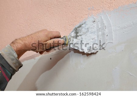 Worker spreading plaster with trowel to gypsum board and fiber mesh