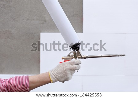 Worker hand holding polyurethane expanding foam glue gun applicator