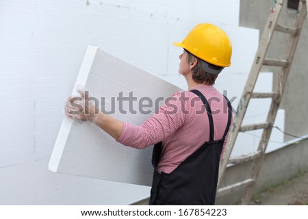 Female worker carrying styrofoam sheet insulation at construction site