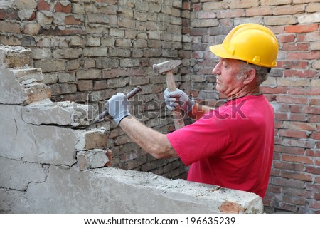 Construction worker demolishing old brick wall with chisel tool and hammer