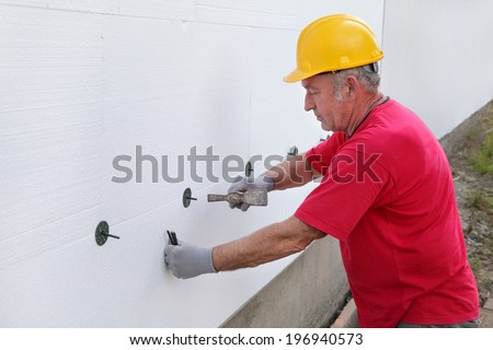 Worker placing expansion anchor to styrofoam sheet insulation of the wall with hammer