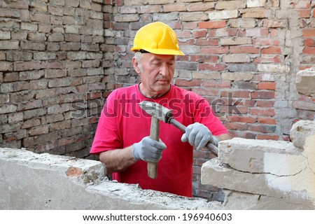 Construction worker demolishing old brick wall with chisel tool and hammer, real people