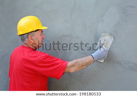 Worker spreading  mortar over styrofoam insulation and mesh  with trowel