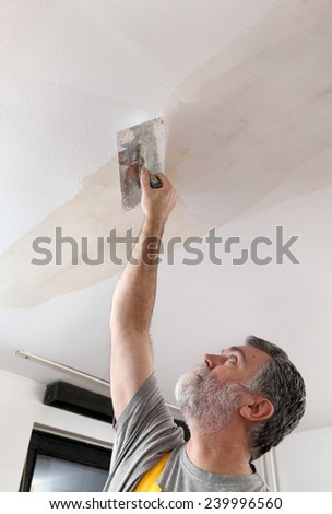 Worker spreading  plaster to ceiling with trowel, repairing works