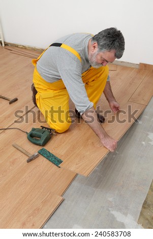 Adult male worker installing laminate floor,  floating wood tile