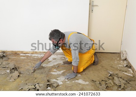 Adult worker with protective mask remove glue and rubber with putty knife from floor