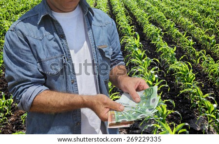 Farmer holding Euro banknote with green cultivated corn field in background
