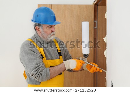Worker install door, using polyurethane foam to fix it at wall