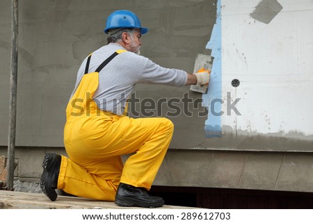Worker spreading  mortar over styrofoam insulation and mesh  with trowel