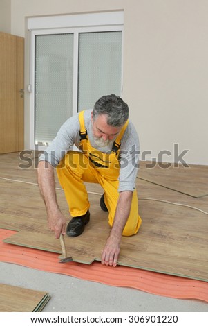 Adult male worker installing laminate floor,  floating wood tile, using hammer