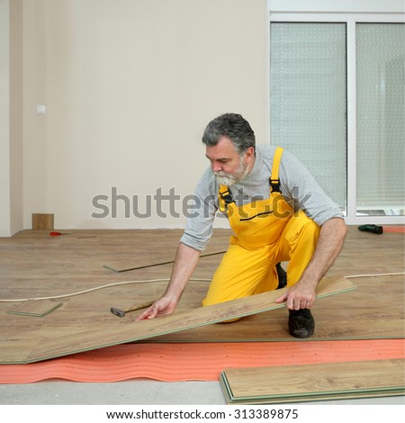 Adult male worker installing laminate floor,  floating wood tile