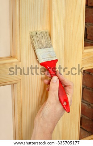 Worker hand painting new wooden door with paintbrush, closeup of varnishing