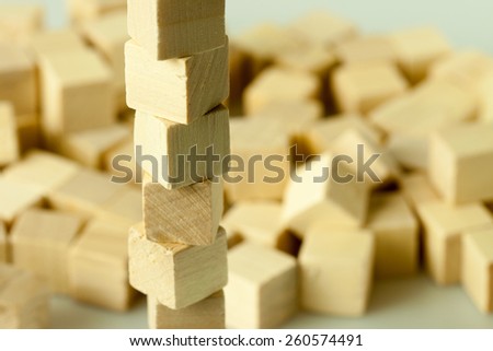 Image of tower structure of rotated and dislocated wooden cubes shot on the background of a heap of other elements from the same kind