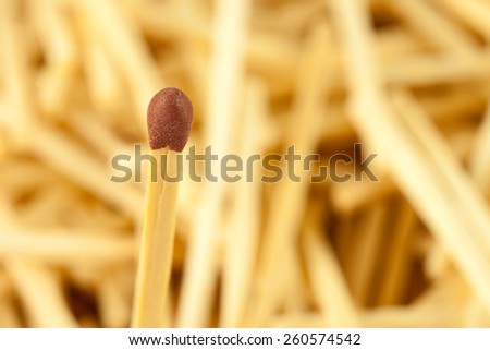 Single matchstick on de-focused background of other wooden sticks symbolizing flammable danger, fire hazard, safety and standing out individuality concept