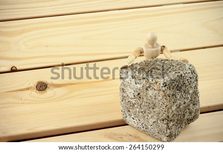 Miniature wooden human model figure pushing heavy granite paving block element towards camera on wood background with vignette effect, symbolizing hard physical Sisyphus labor beyond one\'s strength
