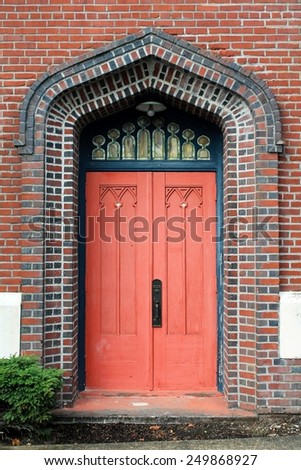 An ornate faded red door with leaded glass panels above set in a colorful brick wall in a historic Pacific Northwest town.
