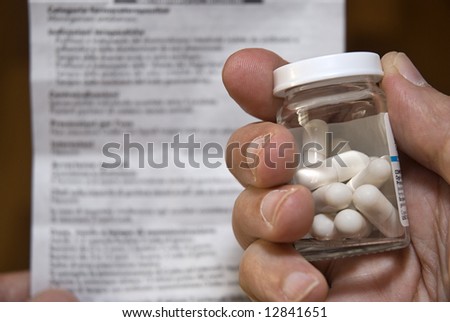 Hand holding a medicine bottle with pills and medical direction paper in the background