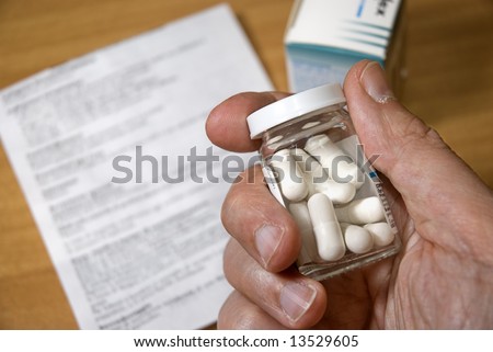 Hand holding a medicine bottle with pills, medical direction paper and medicine box on the table in the background