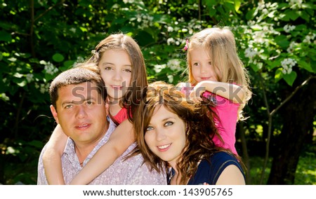 Family from four persons has a rest in a park in shade under trees.