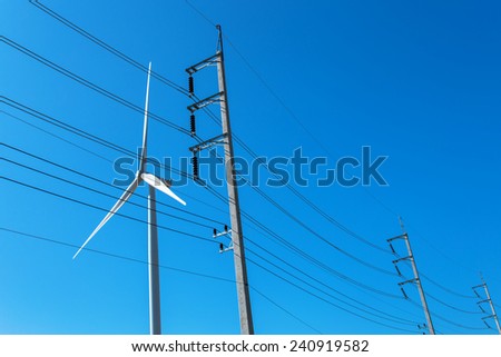 High-voltage tower and wind turbine machine with blue sky background.
