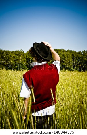 Fashionable man in black hat and red sleeveless among field
