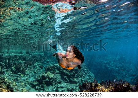 black hair Mermaid swimming underwater in the deep blue sea and looking at you
