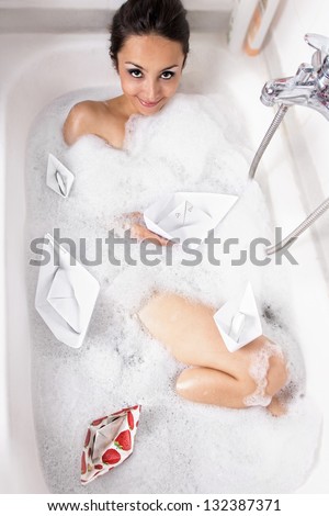 Girl in a bathtub with foam and paper boats