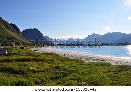 Beautiful beach called Rambergstranden in Lofoten, Norway. Blue sky and blue tagged mountains can be seen in the background.