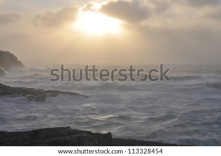 Stormy day in november on the coast of west Norway. Lagre waves and foam . Low sun can be seen  through the clouds.