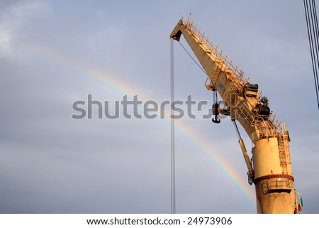 A rainbow on a cloudy sky crosses behind a heavy crane.