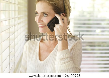 Smiling woman looking out a window while talking on a phone.