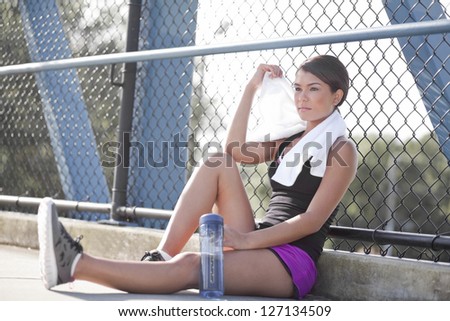An athletic girl sitting and resting to take a break from the sun and heat.