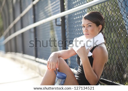 An athletic girl with a determined look on her face while she sits with her water bottle and a towel around her neck.