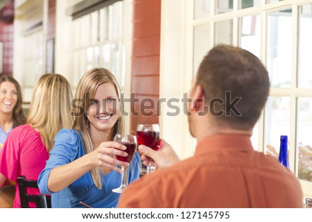 A happy couple toasts with wine at a restaurant with people in the background