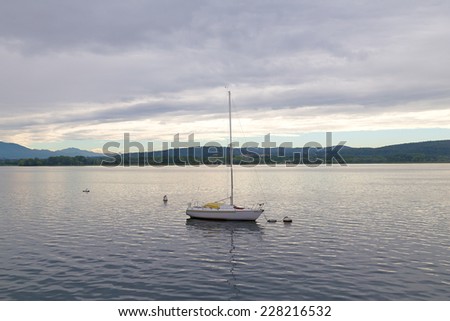 Lonely yacht on Lake Como in Northern Italy. Calm lake waters with yacht and mountains on background.
