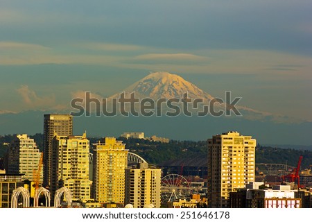 Mount Rainier and Seattle buildings at sunset hours. City view and Mount Rainier with a snow top.