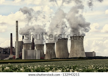 View of coal power plant against sun with several chimneys and huge fumes
