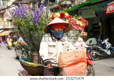 Hanoi, Vietnam - February 6, 2013: A woman is carrying his loaded bicycle with flowers through the crowds of the city of Hanoi, Vietnam.