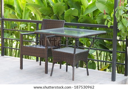 Wicker patio chairs and table near garden.