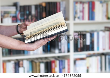 Women\'s hands holding a book in his hand in front of a bookshelf.
