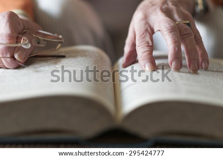 Senior woman reading a book and in her hand she holds a pair of eyeglasses.