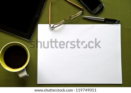 Green desk with coffee, tablet, glasses, phone, pen and a blank paper