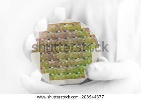 A hi-tech industry engineer in white gloves holding a silicon wafer inside a clean room lab.