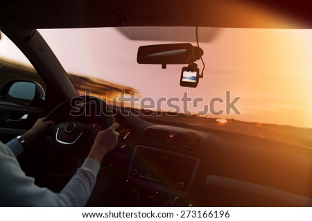 Woman driving a car on highway at sunset, with video recorder next to a rear view mirror